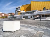 a box sitting in the middle of an empty concrete slab outside a building with a yellow facade