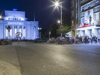 people are standing in line at night at the entrance to an arena with several bikes, and a bike rack on either side
