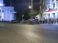 people are standing in line at night at the entrance to an arena with several bikes, and a bike rack on either side