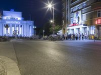 people are standing in line at night at the entrance to an arena with several bikes, and a bike rack on either side