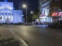 people are standing in line at night at the entrance to an arena with several bikes, and a bike rack on either side