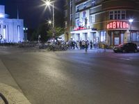 people are standing in line at night at the entrance to an arena with several bikes, and a bike rack on either side
