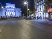 people are standing in line at night at the entrance to an arena with several bikes, and a bike rack on either side