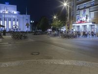 people are standing in line at night at the entrance to an arena with several bikes, and a bike rack on either side