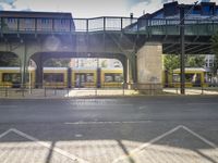 a yellow and white train traveling under the bridge in the city during the day light