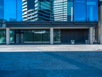 a large blue glass building in the city with a sidewalk and car park area below