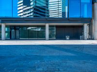 a large blue glass building in the city with a sidewalk and car park area below