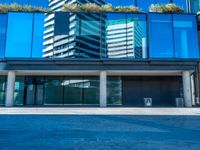 a large blue glass building in the city with a sidewalk and car park area below