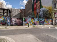 a wall with different colorful artwork on it in a city with buildings around and the street has a bike path going under it