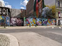 a wall with different colorful artwork on it in a city with buildings around and the street has a bike path going under it