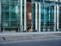 a person walks by a large metal pole near an open brick and glass building with glass walls