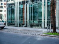 a person walks by a large metal pole near an open brick and glass building with glass walls