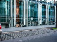 a person walks by a large metal pole near an open brick and glass building with glass walls