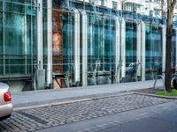 a person walks by a large metal pole near an open brick and glass building with glass walls