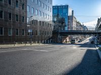 an empty street in an industrial neighborhood with lots of glass buildings on both sides and a bridge in the center