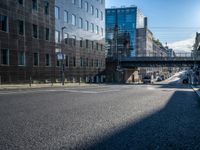 an empty street in an industrial neighborhood with lots of glass buildings on both sides and a bridge in the center