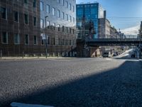 an empty street in an industrial neighborhood with lots of glass buildings on both sides and a bridge in the center