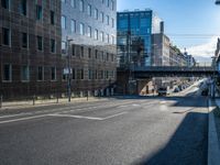 an empty street in an industrial neighborhood with lots of glass buildings on both sides and a bridge in the center