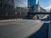 an empty street in an industrial neighborhood with lots of glass buildings on both sides and a bridge in the center