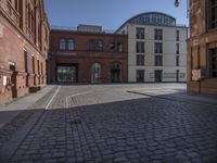 a brick building and clock on a street corner in front of some large buildings and a very long row with tall windows