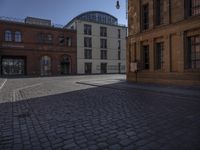 a brick building and clock on a street corner in front of some large buildings and a very long row with tall windows