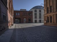 a brick building and clock on a street corner in front of some large buildings and a very long row with tall windows