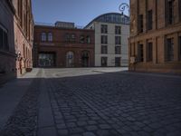 a brick building and clock on a street corner in front of some large buildings and a very long row with tall windows