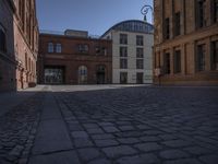 a brick building and clock on a street corner in front of some large buildings and a very long row with tall windows