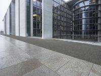 two large tall building next to a walkway with a gated area and glass bales