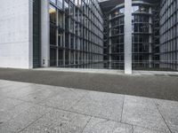 two large tall building next to a walkway with a gated area and glass bales