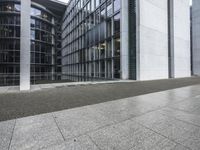 two large tall building next to a walkway with a gated area and glass bales