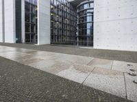 two large tall building next to a walkway with a gated area and glass bales