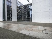 two large tall building next to a walkway with a gated area and glass bales
