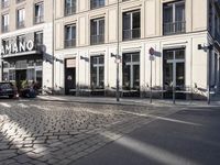an empty cobbled area in front of a tall building with multiple windows and tables