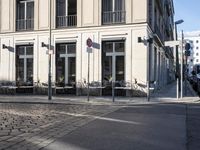 an empty cobbled area in front of a tall building with multiple windows and tables