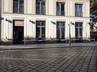 an empty cobbled area in front of a tall building with multiple windows and tables