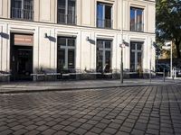 an empty cobbled area in front of a tall building with multiple windows and tables