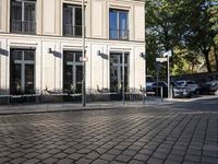 an empty cobbled area in front of a tall building with multiple windows and tables