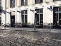 an empty cobbled area in front of a tall building with multiple windows and tables