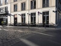 an empty cobbled area in front of a tall building with multiple windows and tables