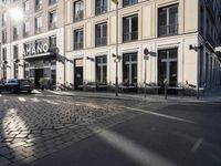 an empty cobbled area in front of a tall building with multiple windows and tables