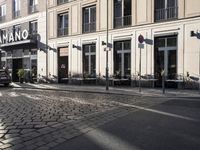 an empty cobbled area in front of a tall building with multiple windows and tables