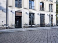 an empty cobbled area in front of a tall building with multiple windows and tables