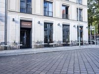 an empty cobbled area in front of a tall building with multiple windows and tables