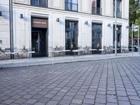an empty cobbled area in front of a tall building with multiple windows and tables