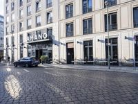 an empty cobbled area in front of a tall building with multiple windows and tables