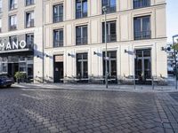 an empty cobbled area in front of a tall building with multiple windows and tables
