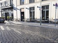 an empty cobbled area in front of a tall building with multiple windows and tables