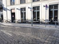 an empty cobbled area in front of a tall building with multiple windows and tables