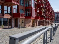 a building with red siding and some balconies in the front of it and a metal bench sitting on the sidewalk outside